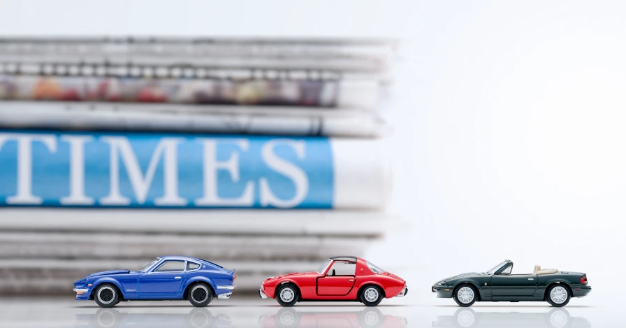 TOMICA OWNER'S CLUB 官方形象圖：一疊印著 TIMES 字樣的報紙前排著三台跑車小車